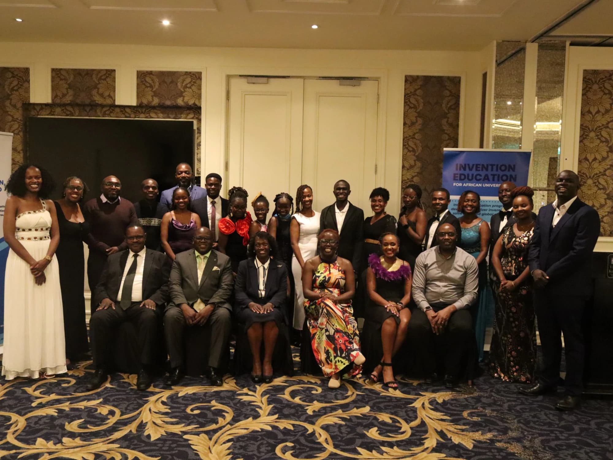 Group photograph at a formal evening event beside an Invention Education banner
