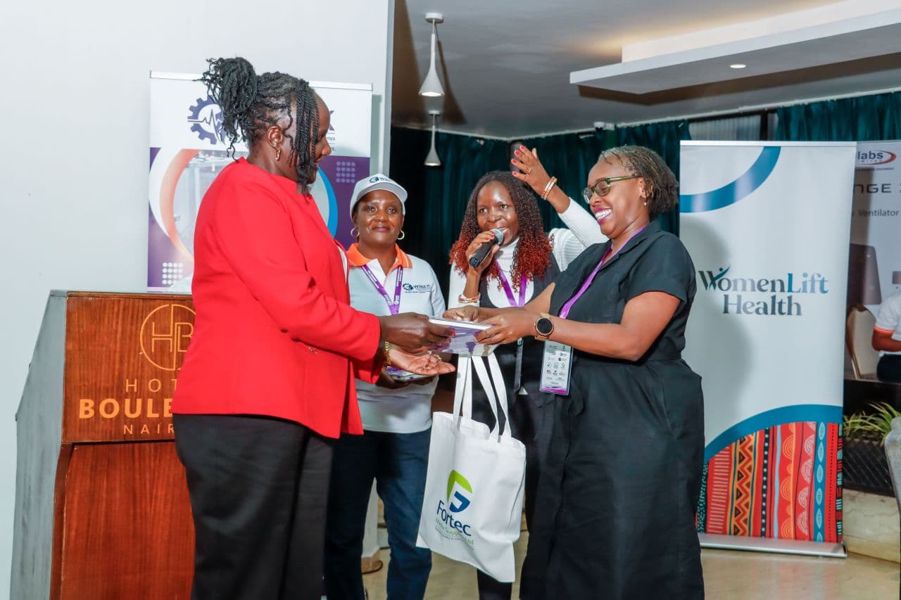 Women holding a gift bag and a microphone on stage beside event banners