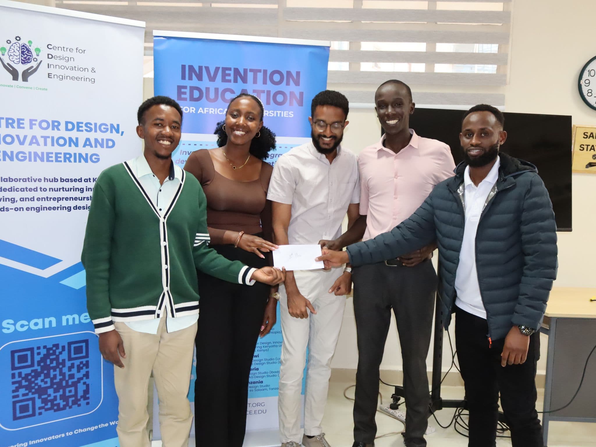 Second-place team of four holding their envelope in front of the Invention Education banner