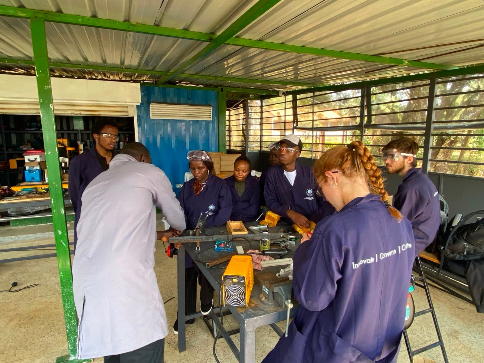 An instructor demonstrating at a metalwork bench while participants in CDIE coats watch