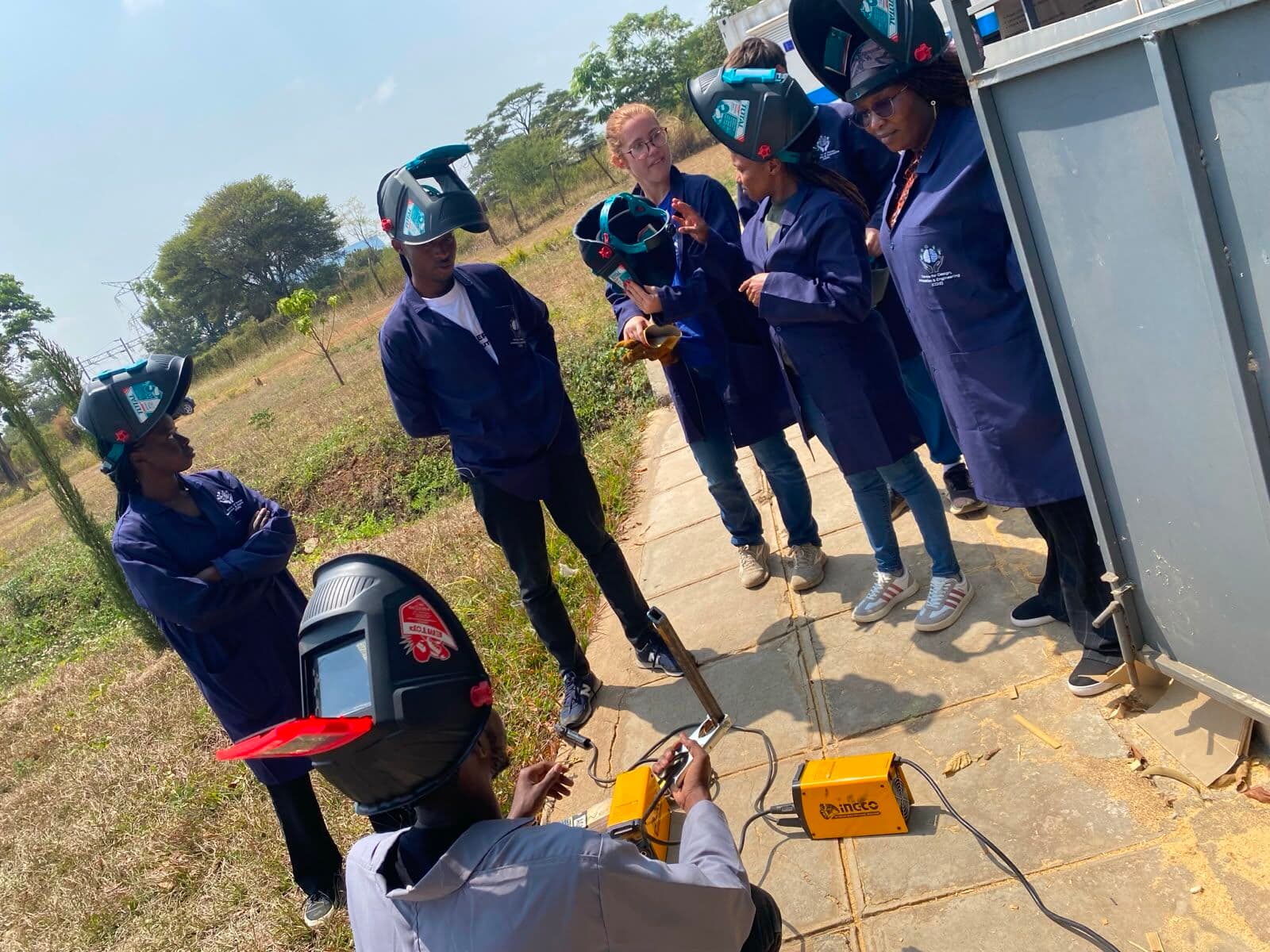 Participants in welding helmets watching an arc welding demonstration outside the workshop