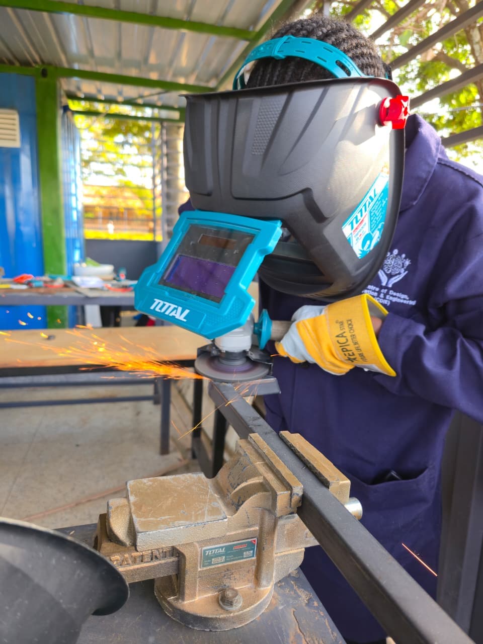 Student in a welding helmet grinding metal as sparks fly