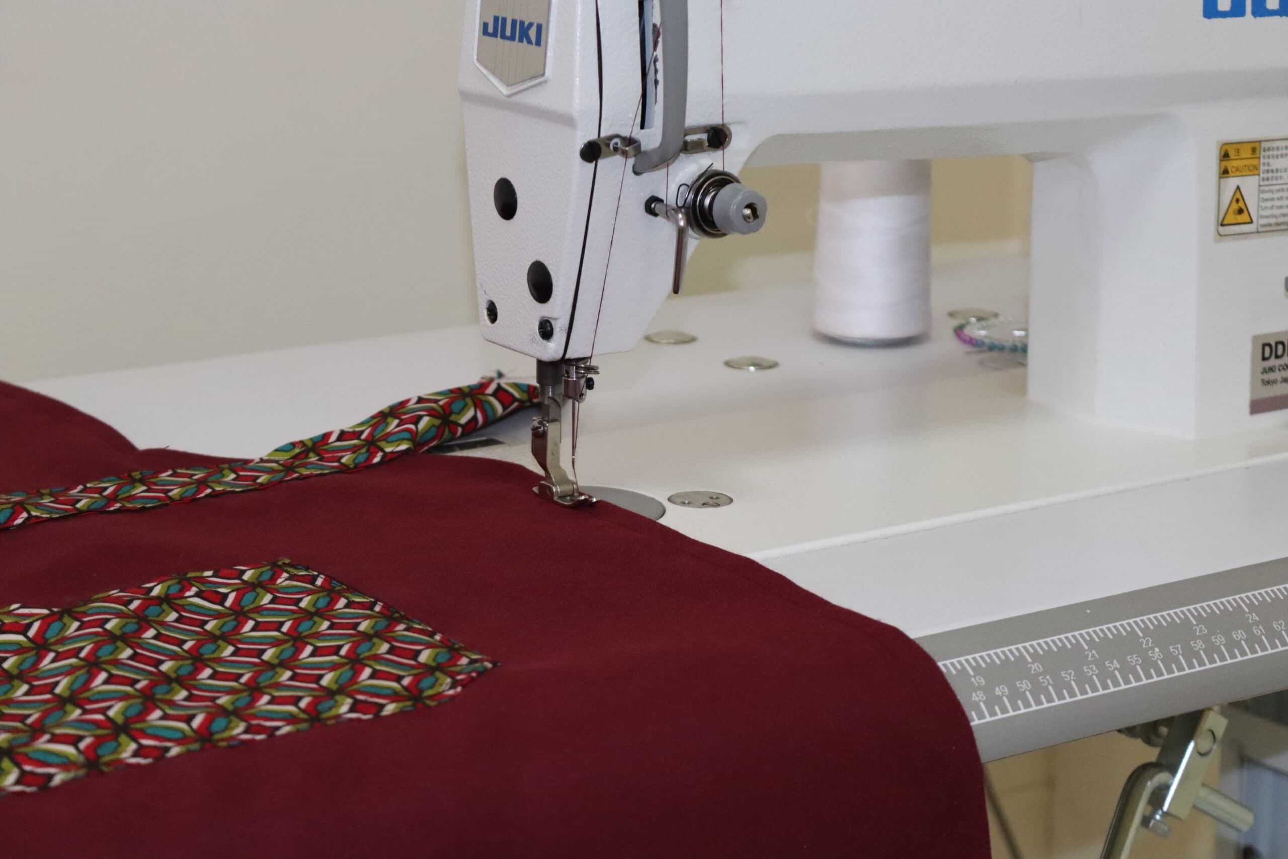 Industrial sewing machine stitching patterned trim onto maroon fabric