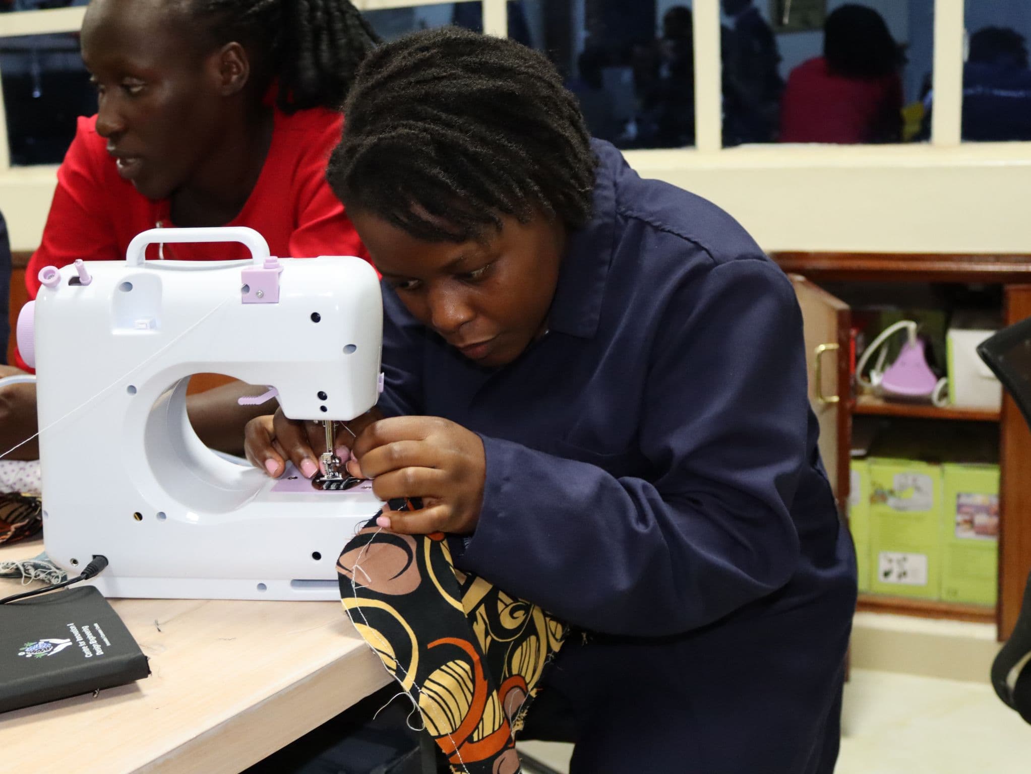 A participant guiding fabric through a sewing machine in the textiles class