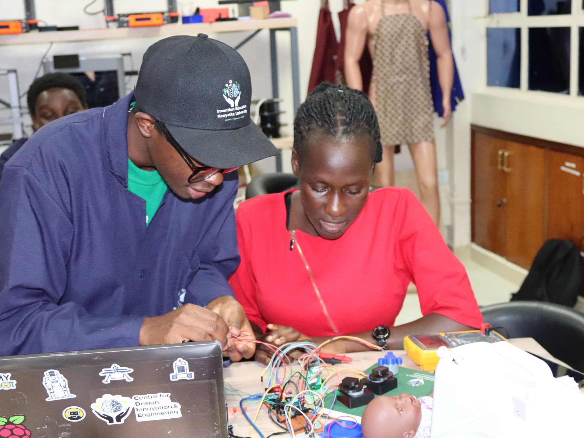 Two participants wiring a breadboard prototype at the electronics bench